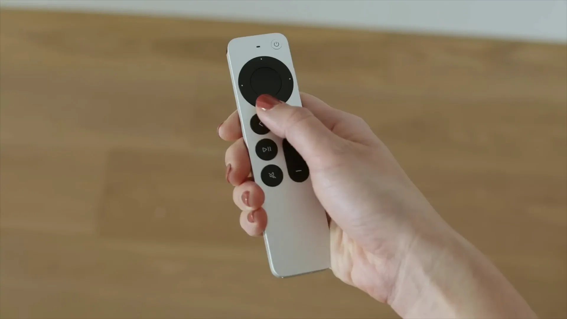 Person holding a silver Apple TV Siri remote with their thumb resting on the clickpad