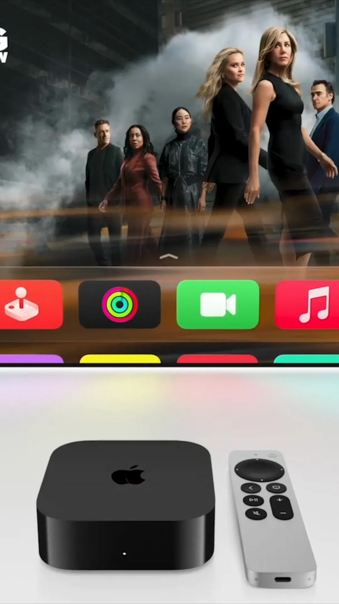 A black square Apple TV set-top box and a silver remote resting below a television screen showing a menu