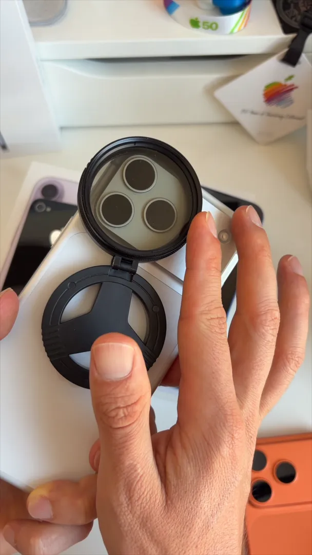 Black circular clip-on solar filter attached over the camera lenses on the back of a white iPhone