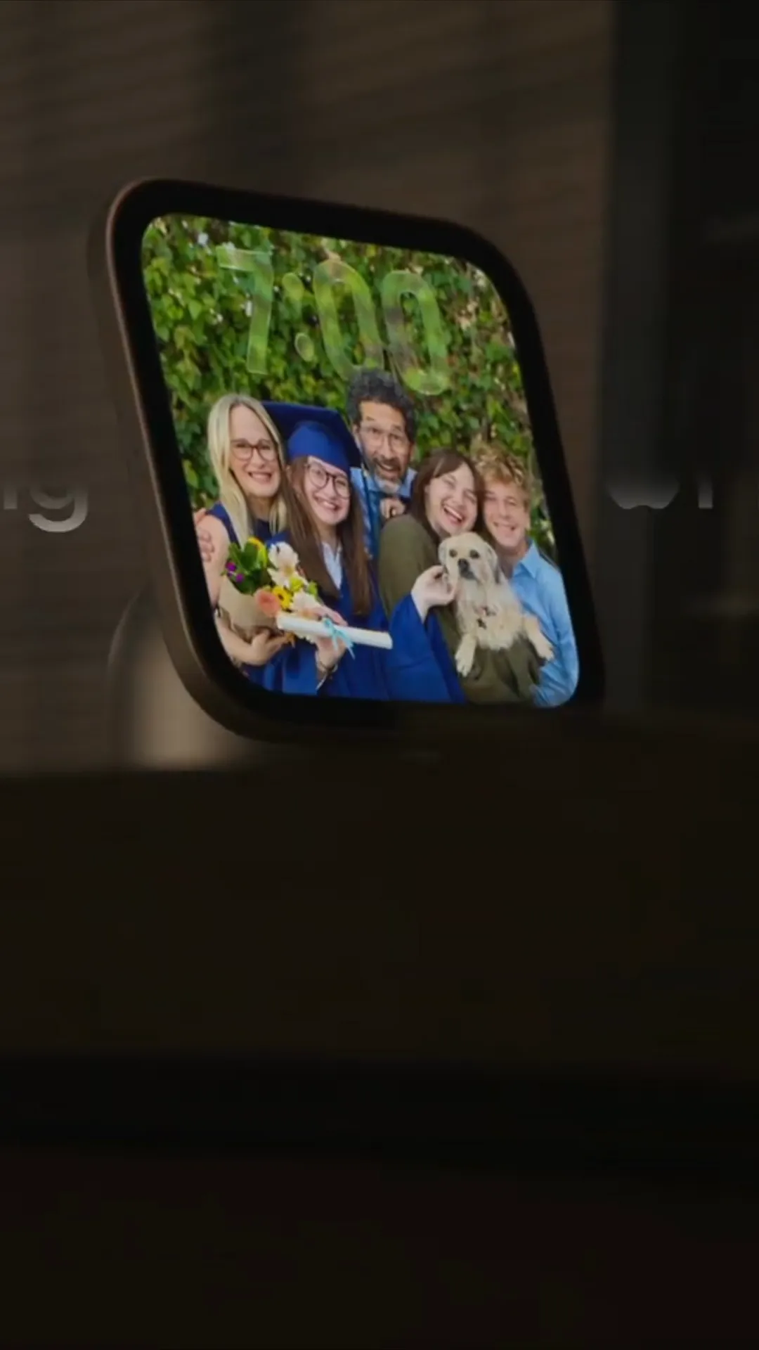 A small silver smart display showing a family photo on its screen, resting on a desk surface