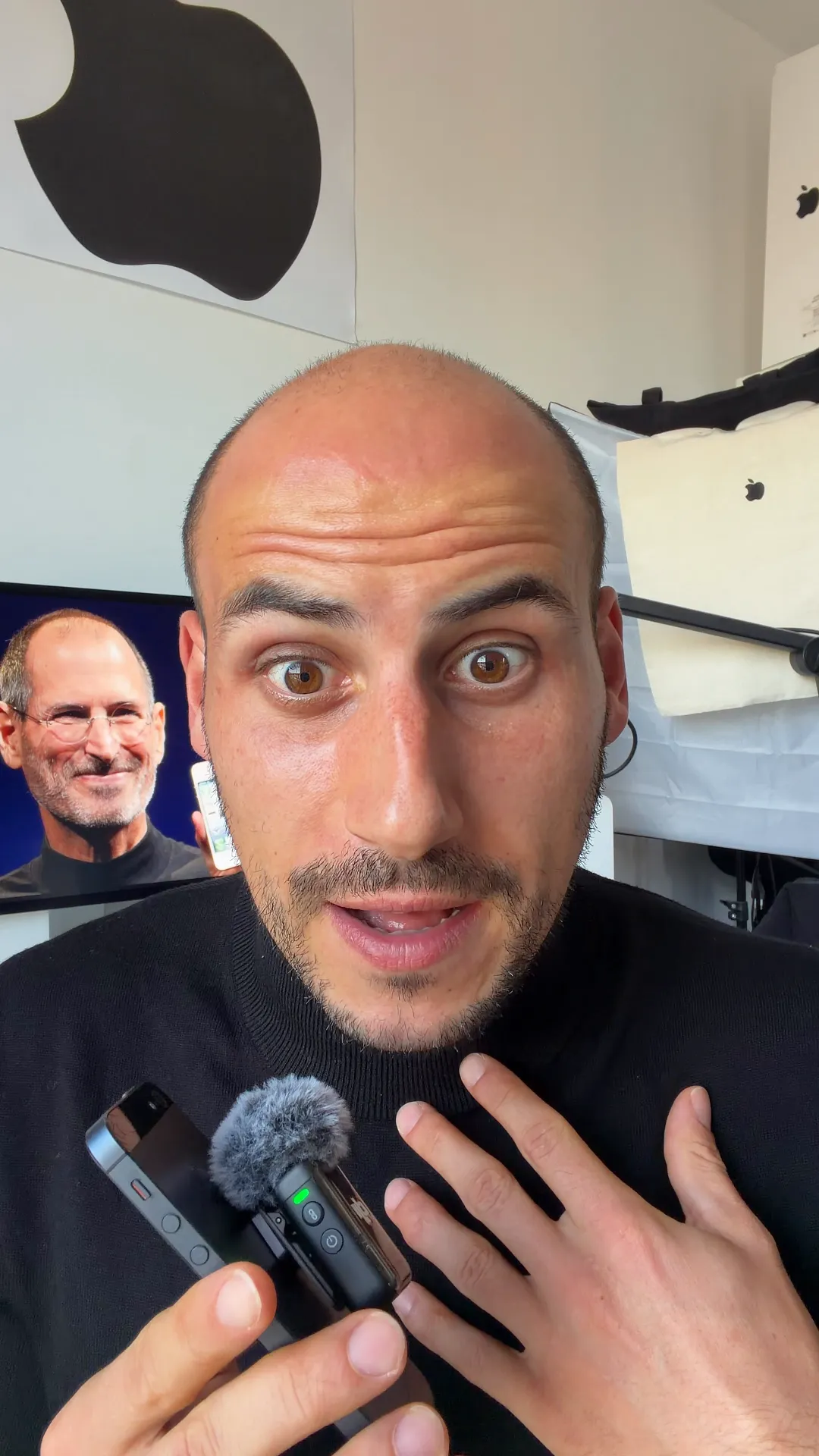 Man holding a small microphone in front of a monitor displaying Steve Jobs